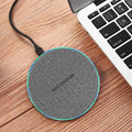 "Gray circular wireless charger placed on a wooden surface beside a laptop, professional workspace accessories for tech-savvy users."