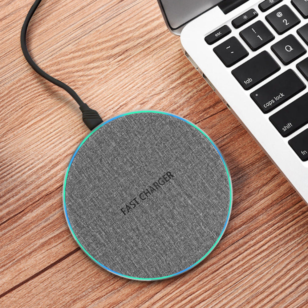 "Gray circular wireless charger placed on a wooden surface beside a laptop, professional workspace accessories for tech-savvy users."