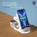 Three-in-one wireless fast charging charger with smartphone, watch, and headphones on a wooden surface.